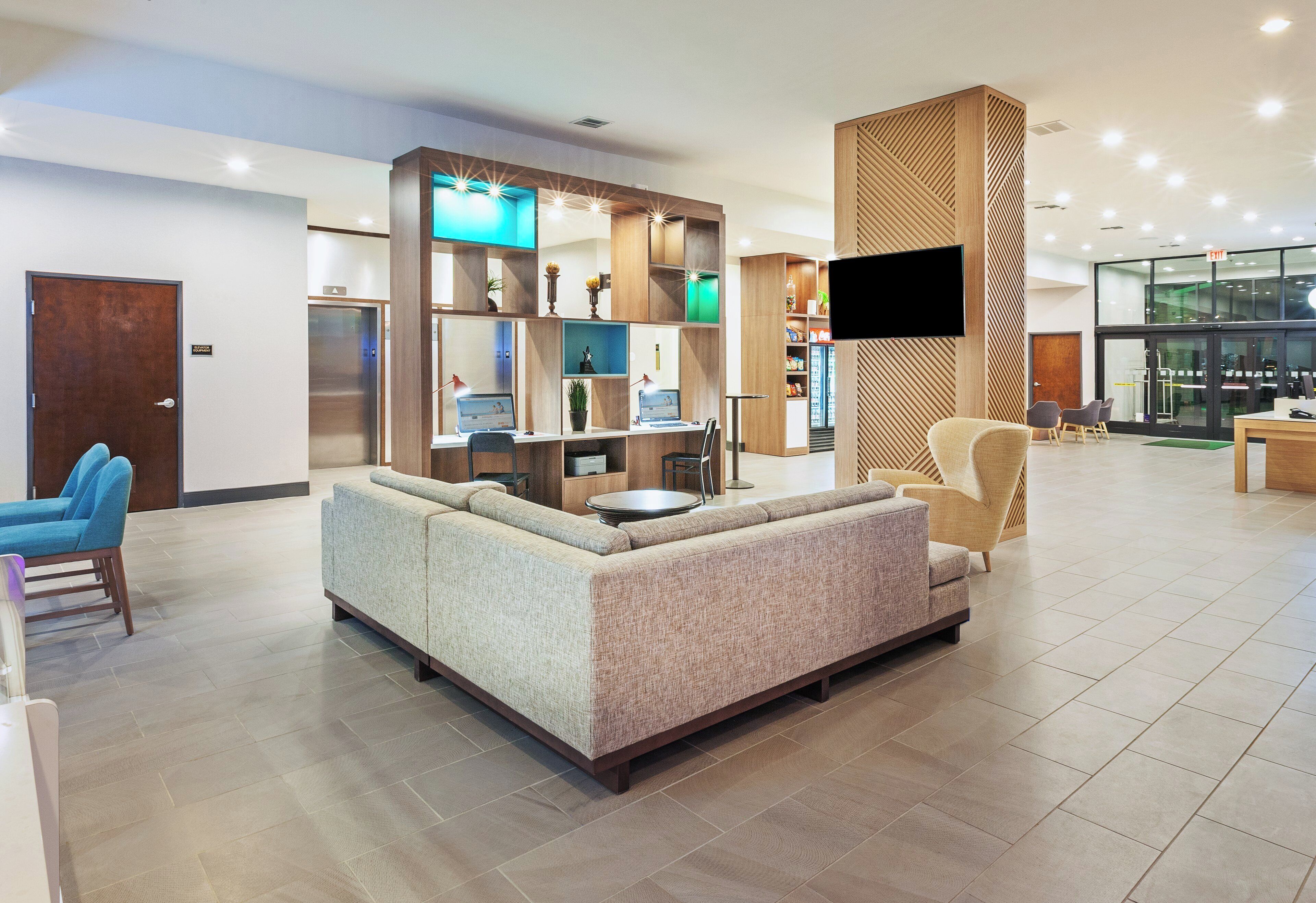 Un vestíbulo moderno con un sofá, sillas, una mesa de recepción y una pantalla de televisión.