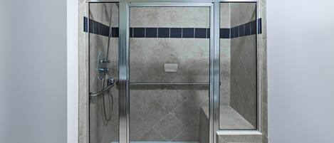 Une cabine de douche fermée par des parois en verre, dotée d’un sol carrelé et d’un pommeau de douche.