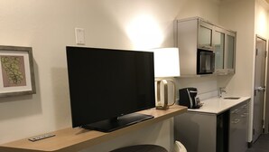 Ein Hotelzimmer mit Fernseher auf einem Holztisch, einem kleinen Tisch mit Stuhl, einer Küchenzeile mit Mikrowelle und einer Kaffeemaschine.