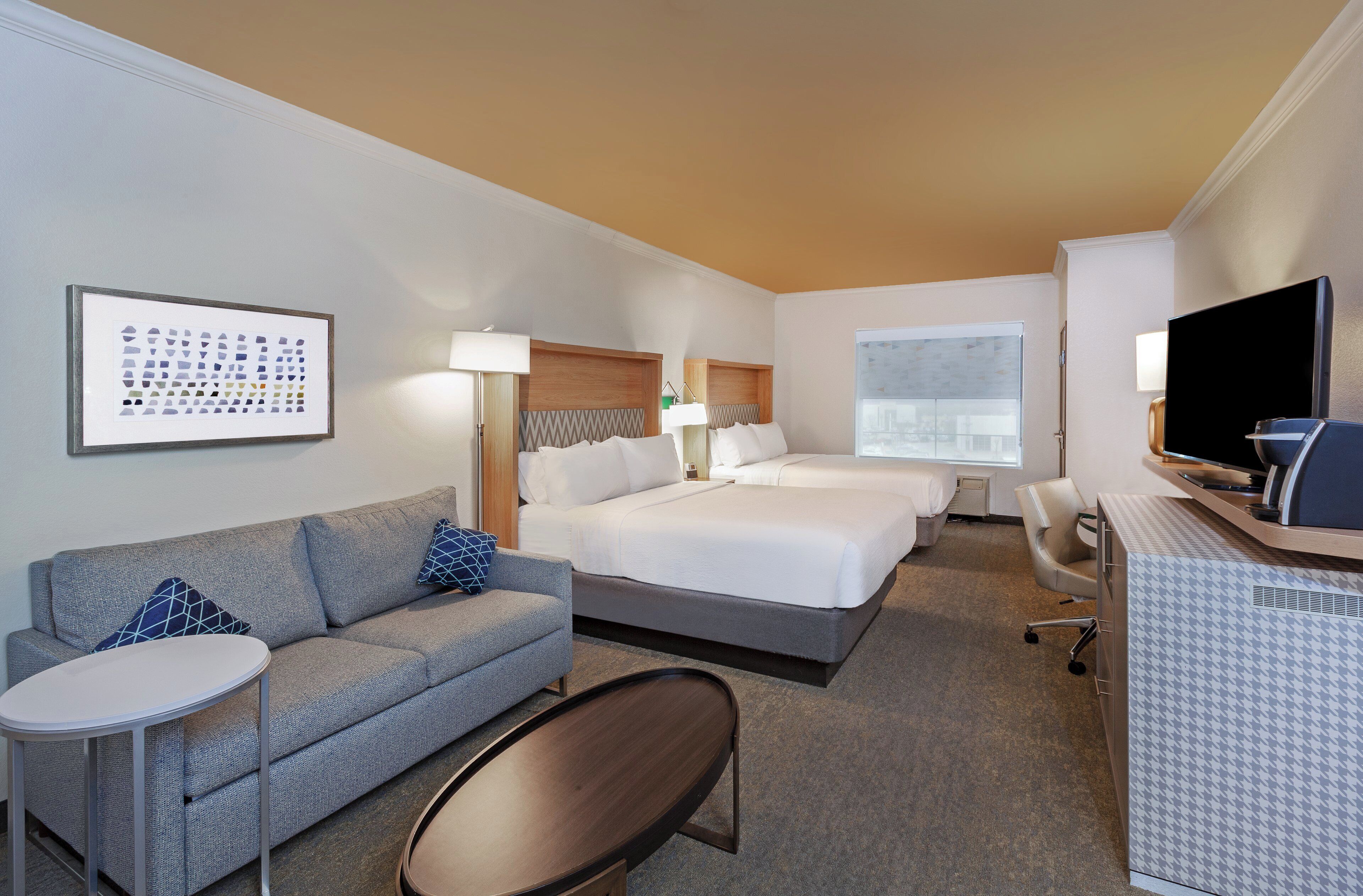 A hotel room with a bed, a sofa, a desk, a TV, and a window.
