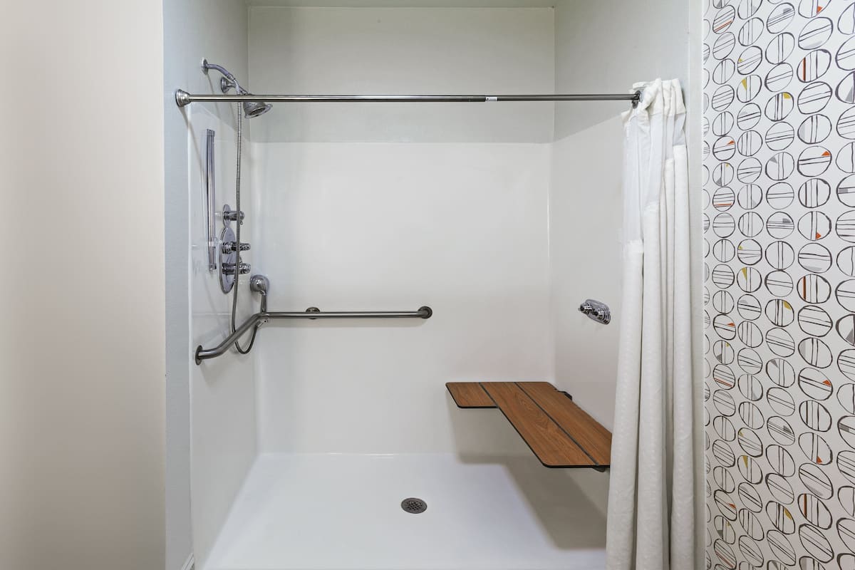 A shower with a wooden shelf, a grab bar, and a shower curtain.