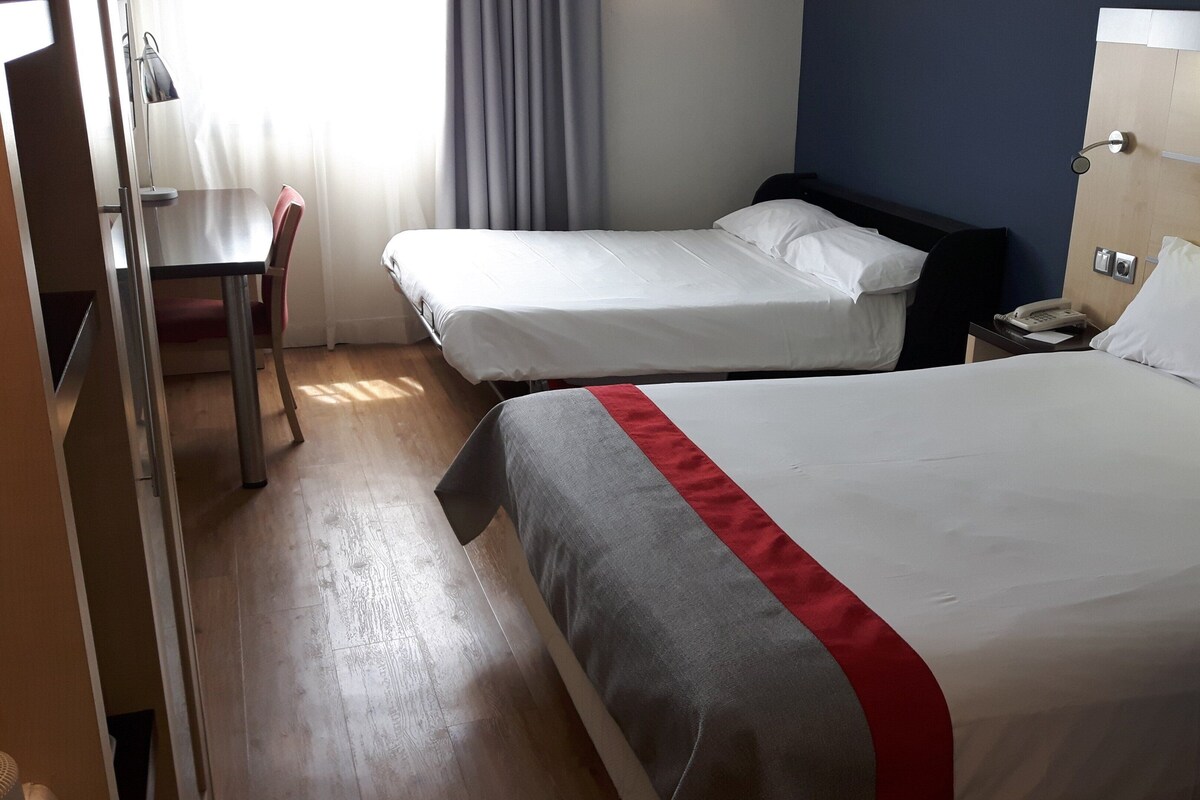 A hotel room with two beds, a desk, and a chair.