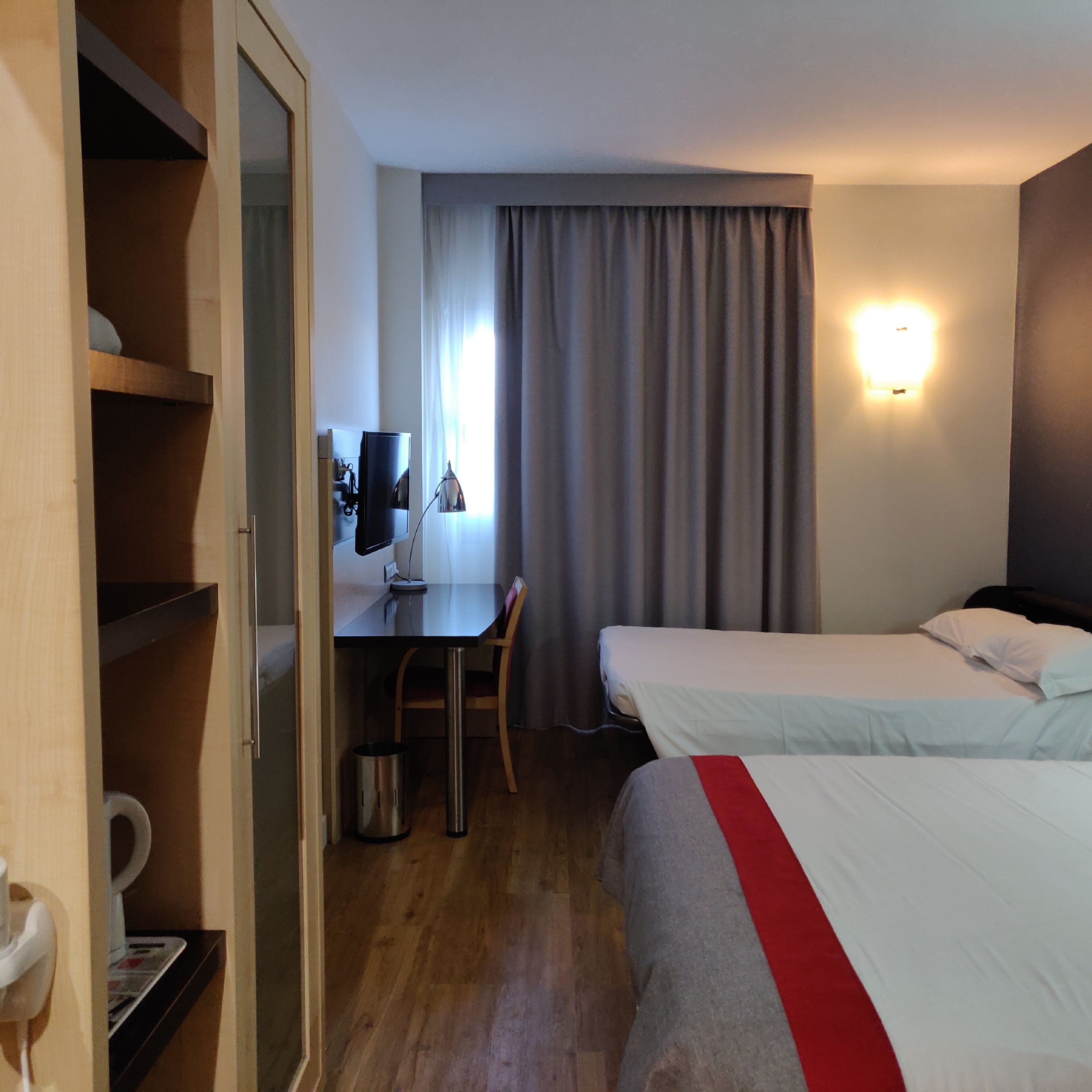 A hotel room with a desk, chair, two beds, and a wardrobe.