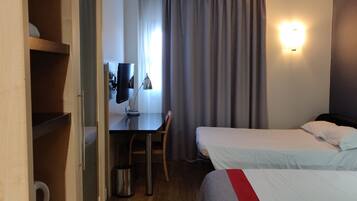 A hotel room with a desk, chair, two beds, and a wardrobe.