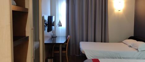 Habitación de hotel con escritorio, silla, dos camas y armario.