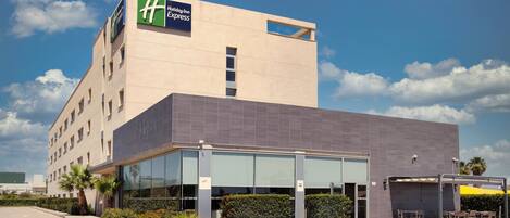 A Holiday Inn Express building with a modern design, large windows, and a parking area with outdoor seating.