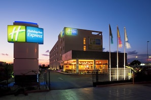 A Holiday Inn Express hotel with a prominent sign, a modern building facade, and multiple flags. - Holiday Inn Express Malaga Airport by IHG (Málaga)