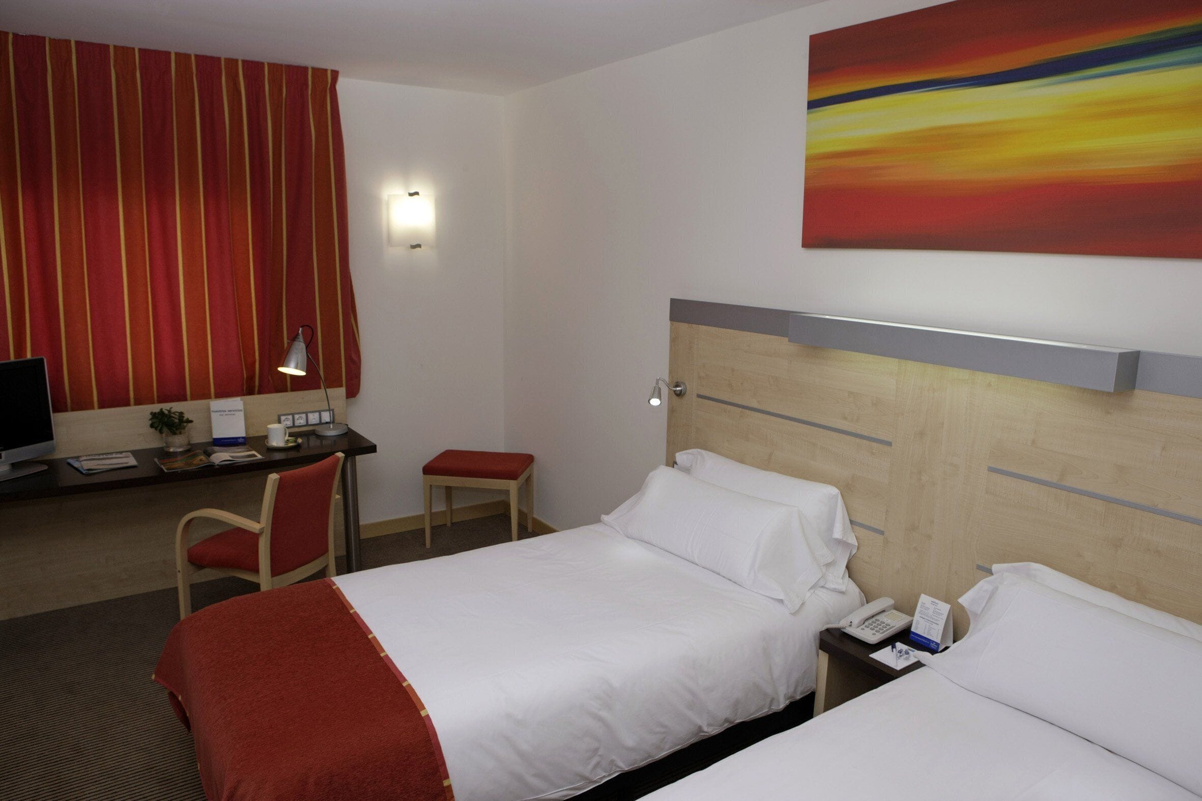 Ett hotellrum med en säng, ett skrivbord med en dator, en stol och ett litet bord.