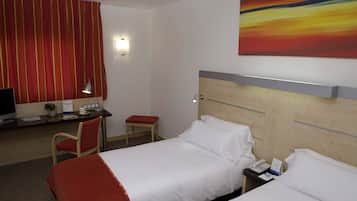 A hotel room with a bed, a desk with a computer, a chair, and a small table.