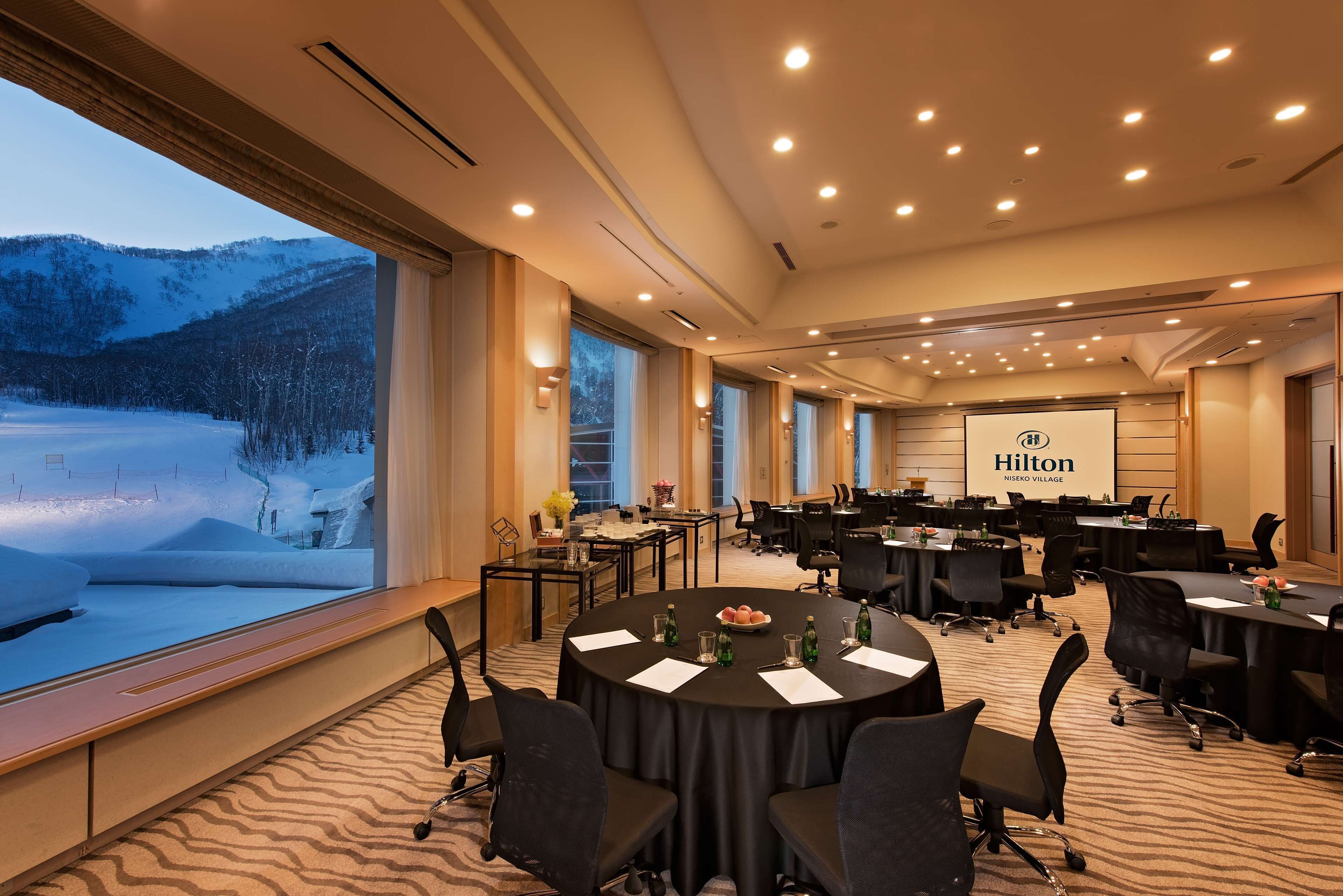 A conference room with round tables, chairs, and a large screen displaying the Hilton logo.