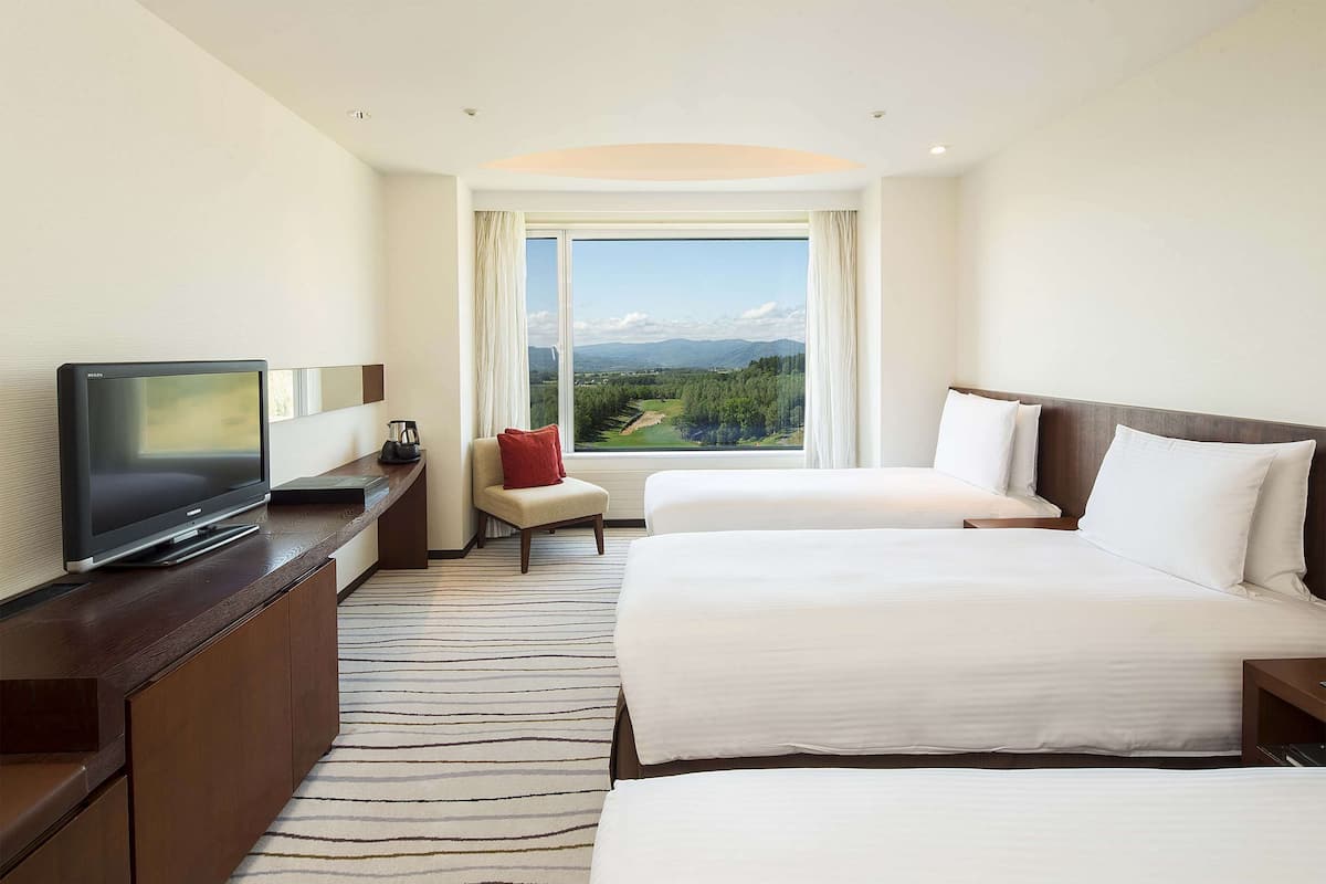 Ein Hotelzimmer mit zwei Betten, einem Fernseher, einem Sessel und einem großen Fenster mit Landschaftsblick.