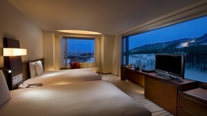 A hotel room with two beds, a TV, a desk, and a large window with a mountain view.