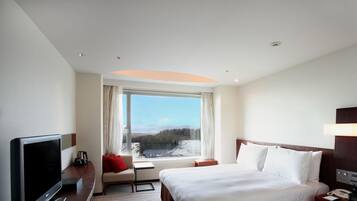 Habitación de hotel con cama, televisión, escritorio, ventana con vista a un paisaje nevado y una lámpara en el techo.