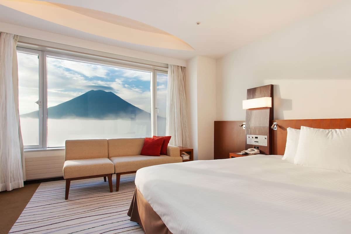 Ein Hotelzimmer mit einem großen Bett, einem Schlafsofa, einem Nachttisch und Blick auf einen Berg durch das Fenster.