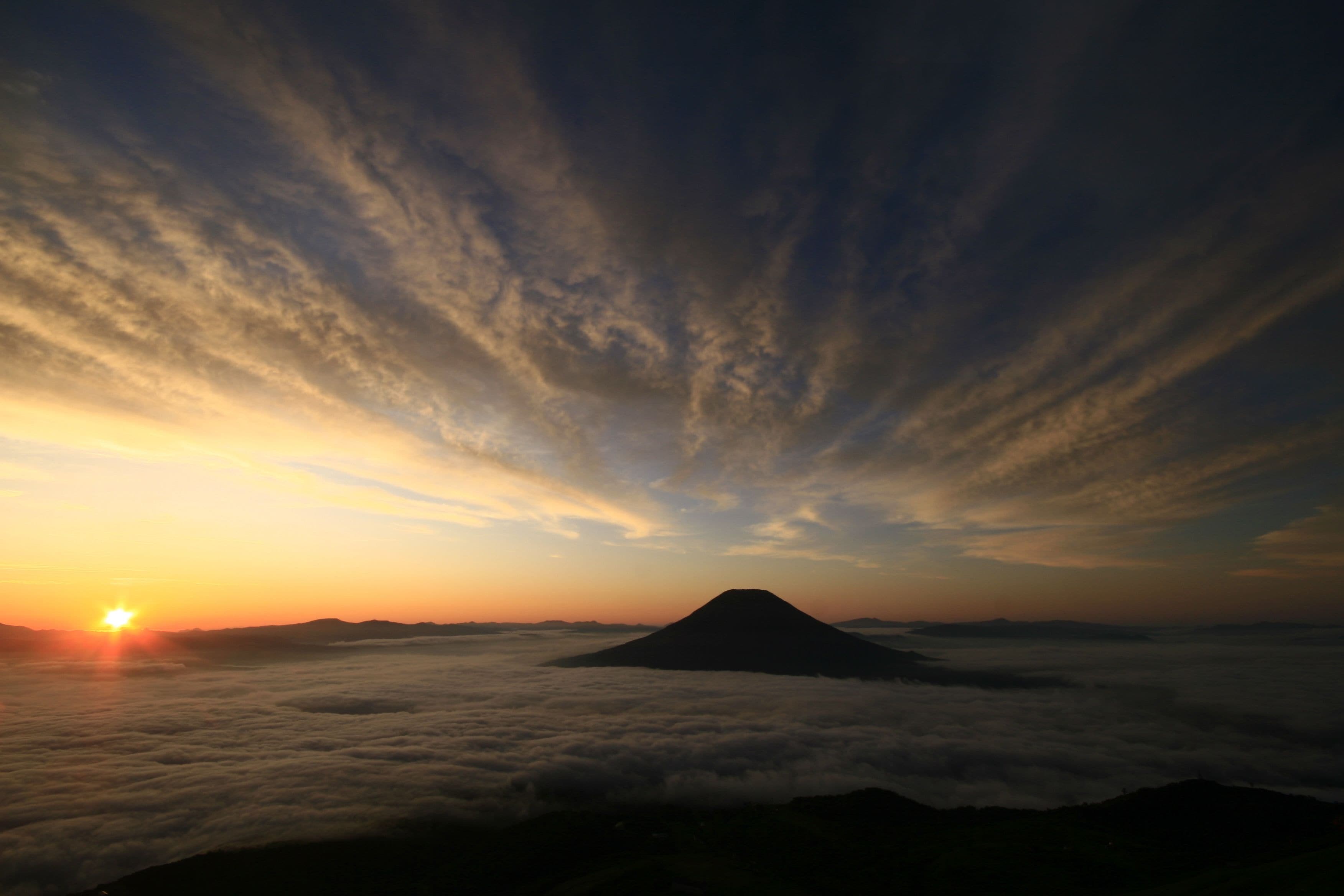 A mountain at sunrise with clouds below.