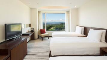Habitación de hotel con televisión, escritorio, dos camas, una silla y un amplio ventanal con vistas al campo.