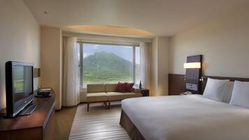 A hotel room with a large bed, a TV, a desk, a window with a mountain view, and a nightstand.