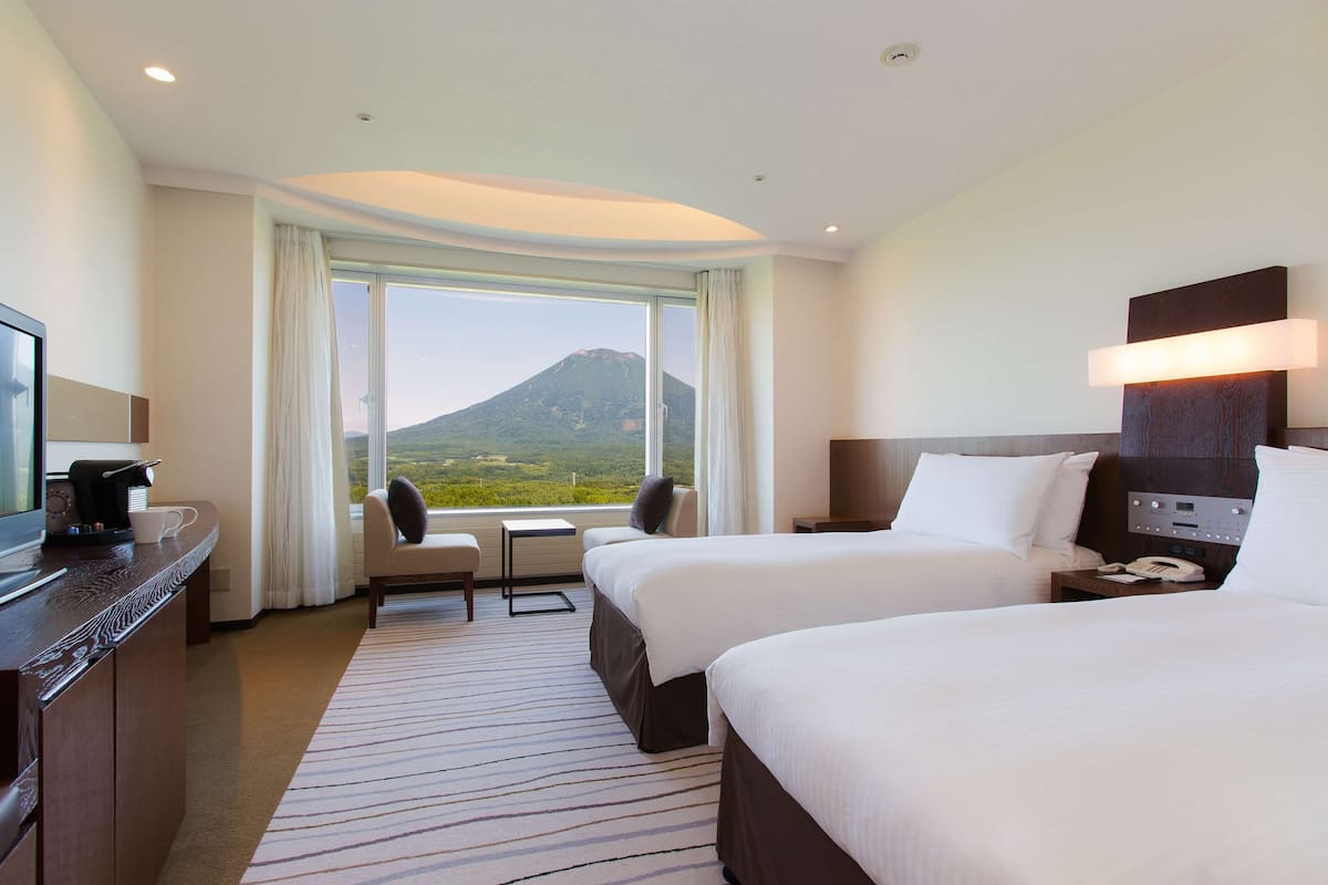 Ein Hotelzimmer mit zwei Betten, einem Schreibtisch mit Kaffeemaschine, einem Sessel und Bergblick.