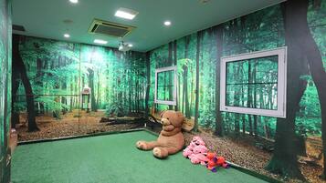 A room with a forest-themed mural, a large teddy bear, and a window.
