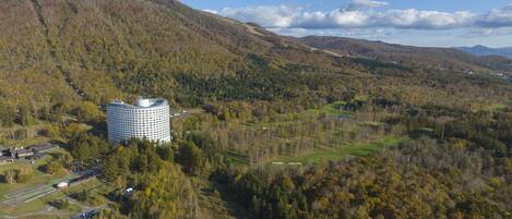 A large hotel with a circular design, surrounded by a forested landscape and hills.