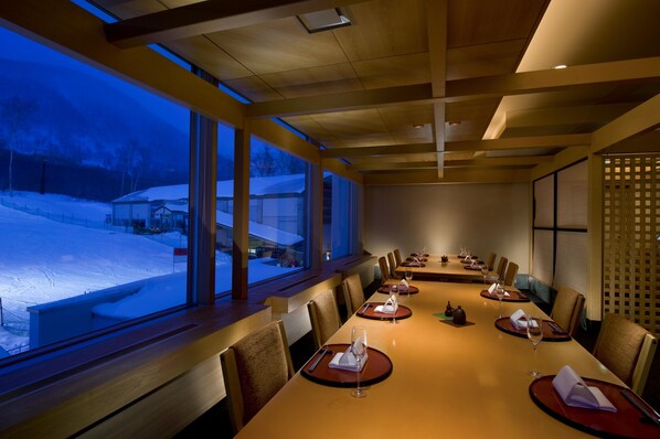 A conference room with a long table, chairs, and a view of a snowy landscape through large windows. - Hilton Niseko Village (Niseko)