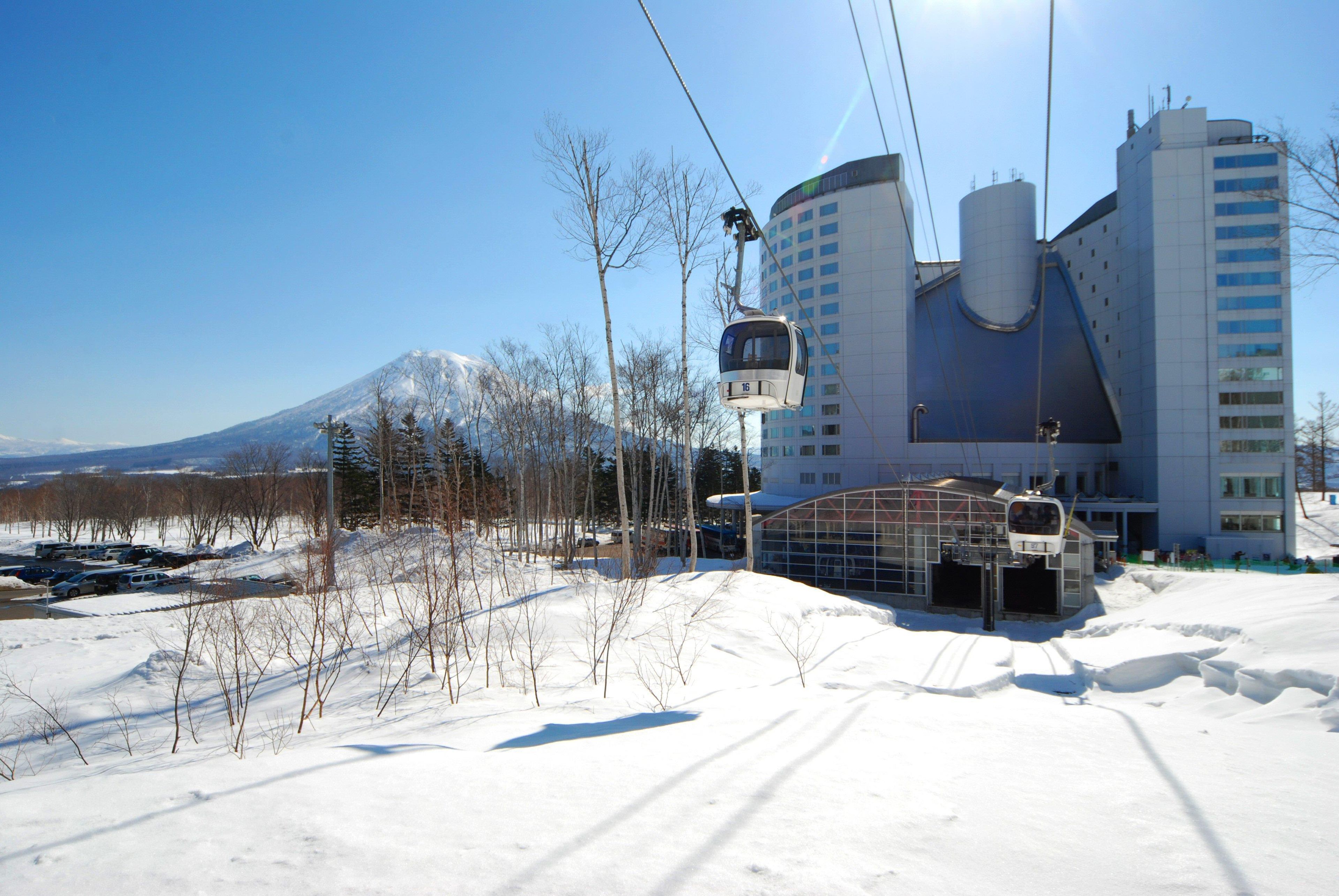 A cable car station with a cable car numbered 16, a modern building with a curved facade, and a snow-covered landscape with trees.
