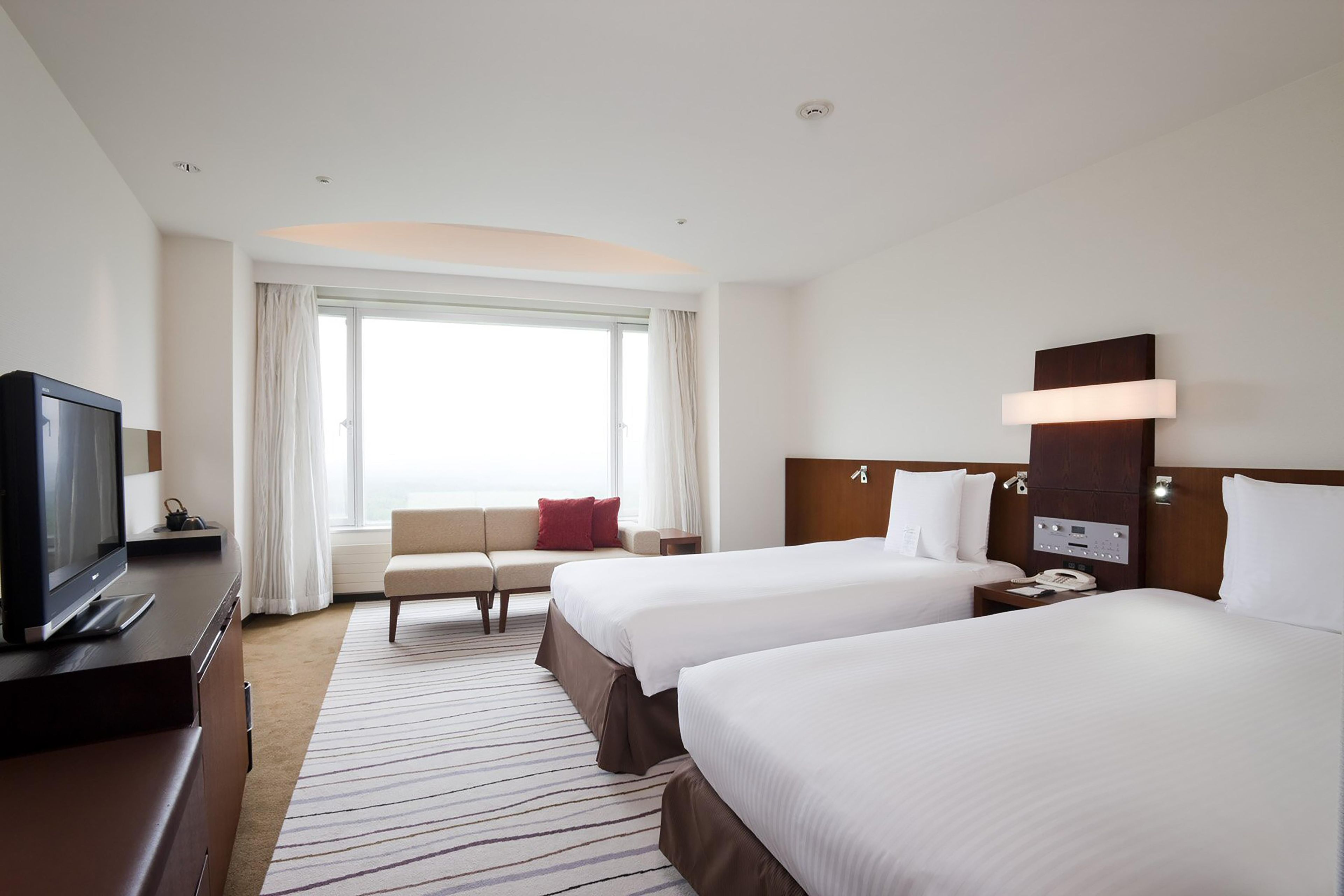 A hotel room with two beds, a sofa, a TV, and a window with curtains.
