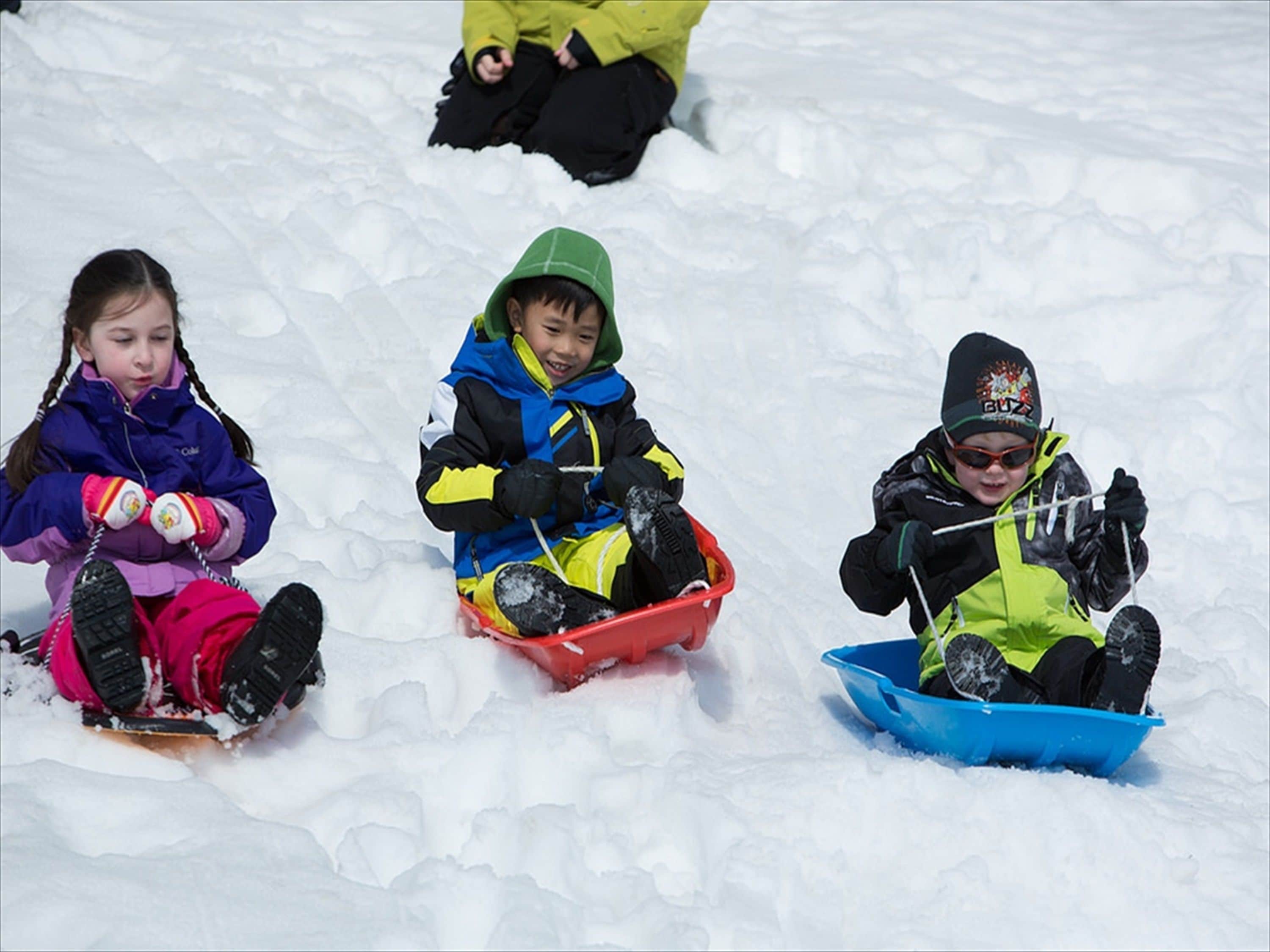 Tres niños deslizándose en trineos por la nieve.