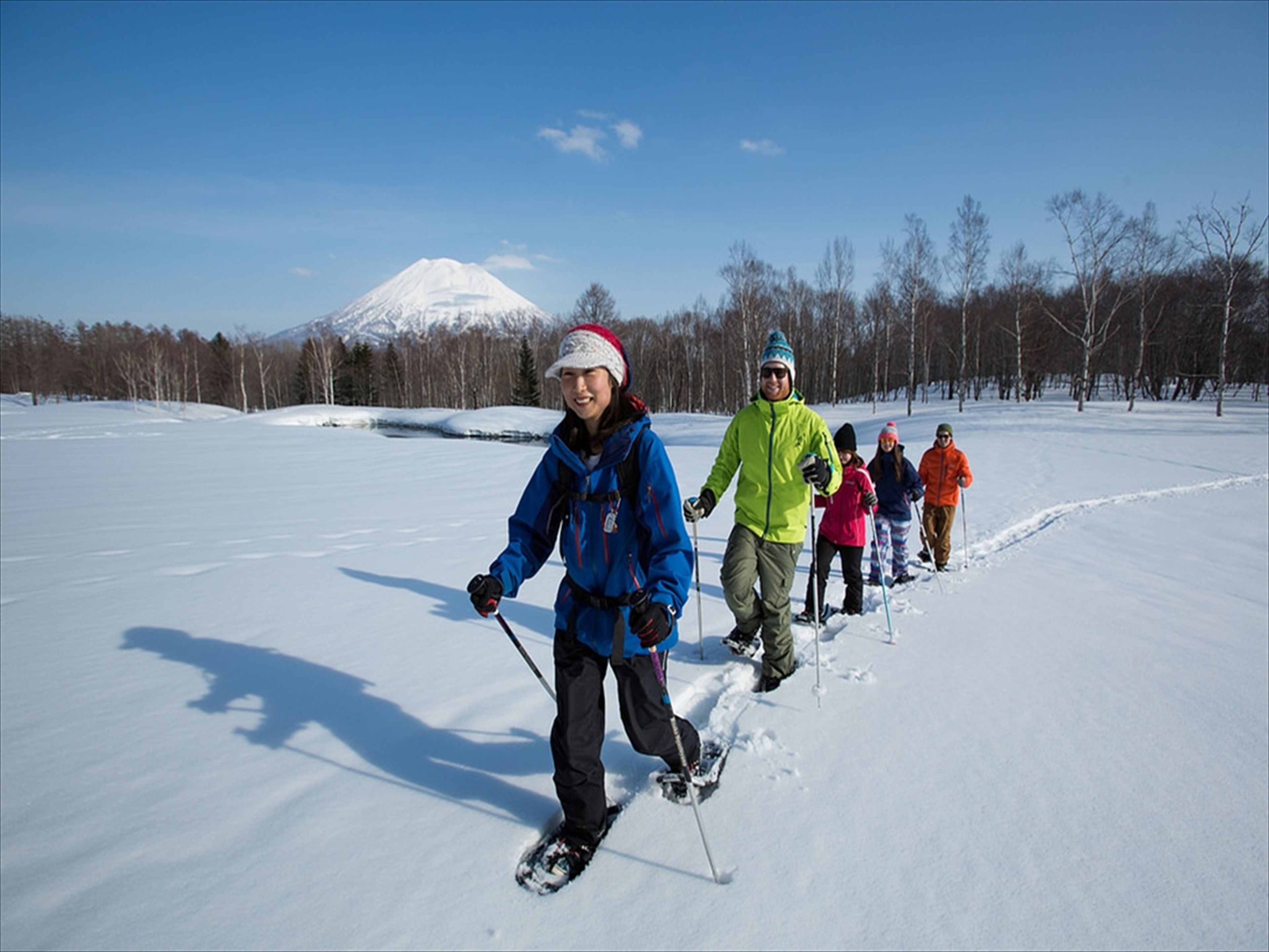 A group of people cross-country skiing on a snowy landscape with a mountain in the background.