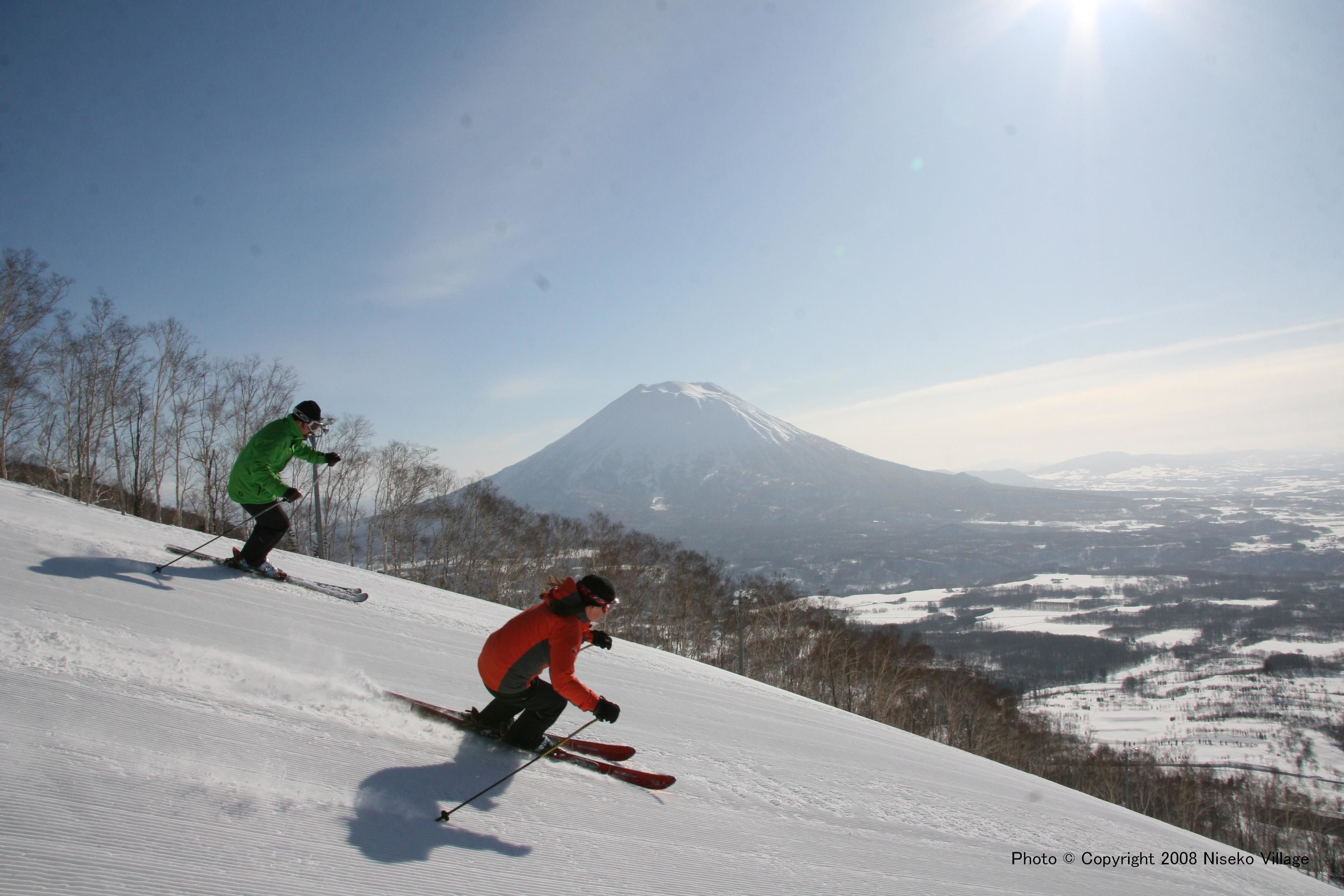 Two skiers on a snowy slope with a mountain in the background.