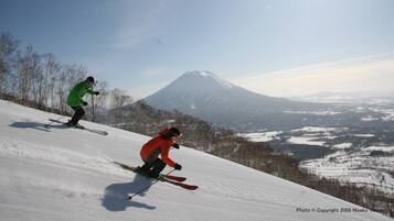 Two skiers on a snowy slope with a mountain in the background.