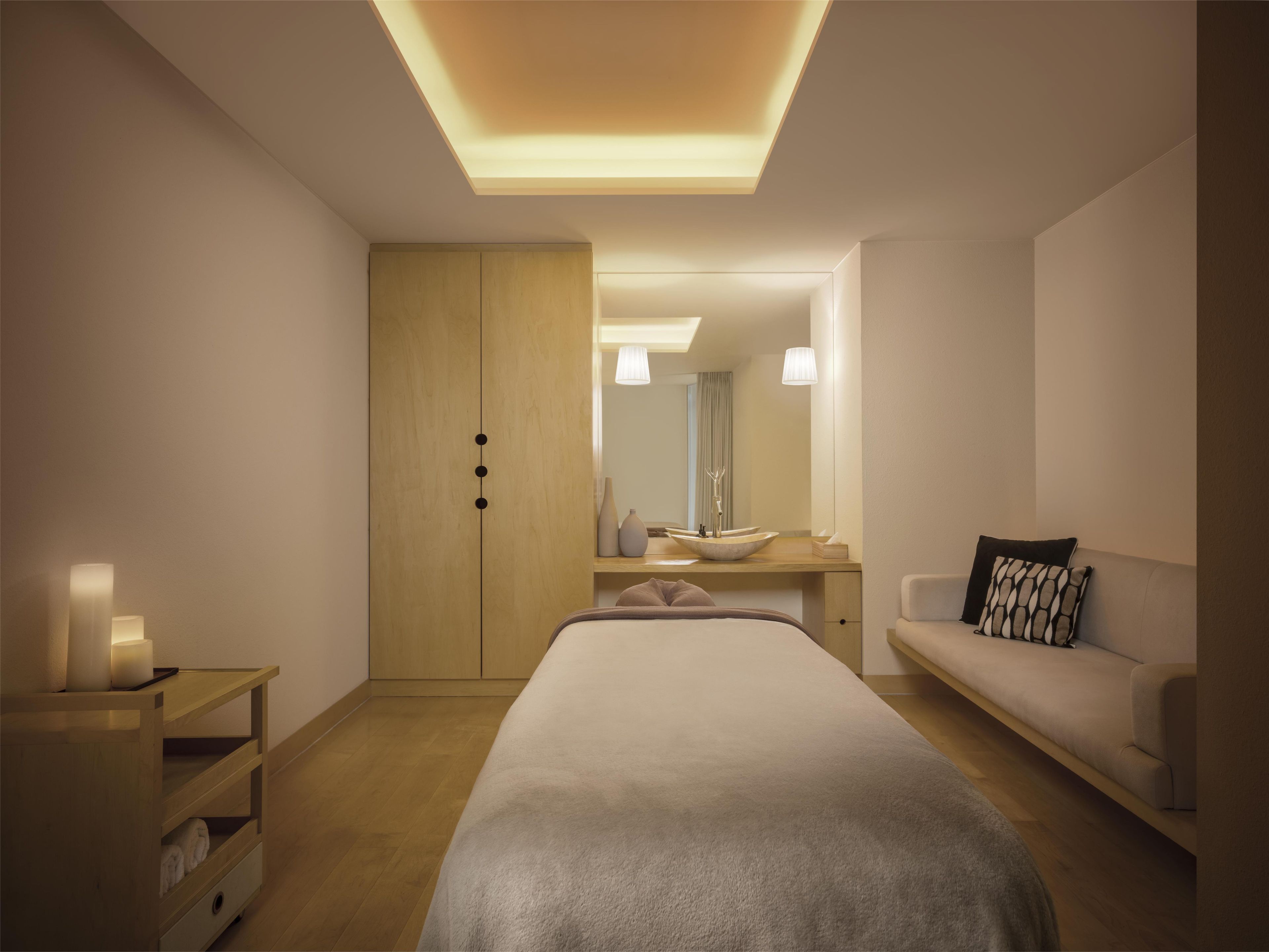 Een moderne slaapkamer met een bed, een houten garderobe, een nachtkastje met een lamp, een spiegel en een bank.