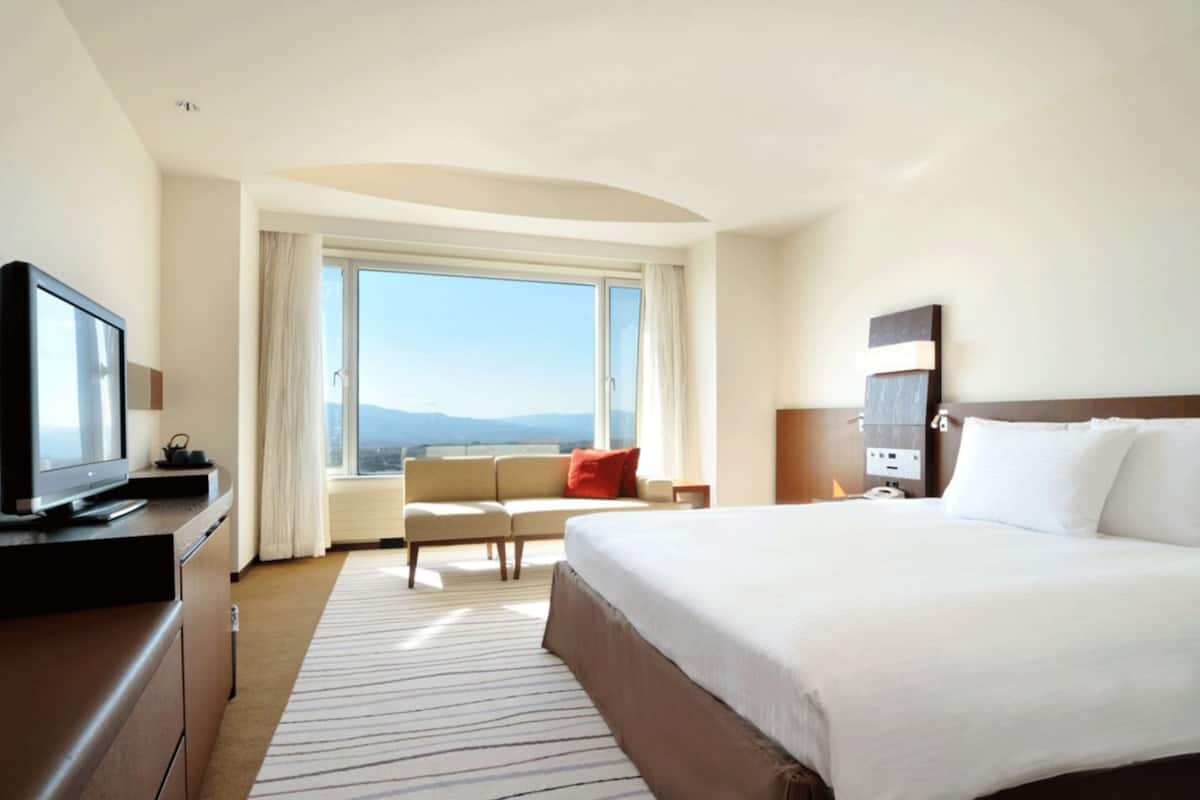 Ein Hotelzimmer mit einem großen Bett, einem Fernseher, einer Sitzecke und Blick auf die Berge.