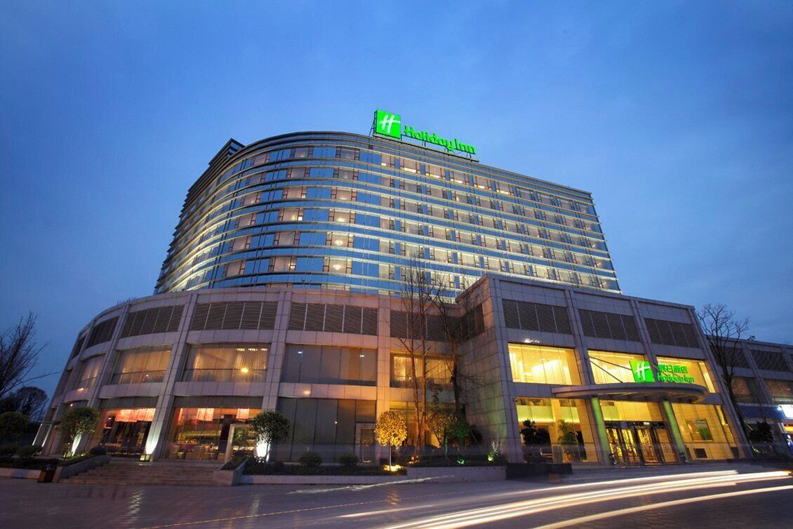 Ein mehrstöckiges Hotel mit einer geschwungenen Fassade, großen Fenstern und einem auffälligen grünen Logo.