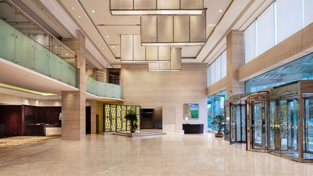Un hall d’entrée spacieux avec un plafond haut, des portes d’ascenseur en verre et un comptoir d’accueil.