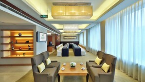 Un hall d’hôtel comprenant un comptoir d’accueil, une longue table à manger entourée de chaises, des canapés et un lustre.