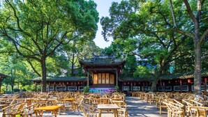 Un pavillon chinois traditionnel, entouré d’arbres luxuriants et agrémenté de mobilier en bambou.