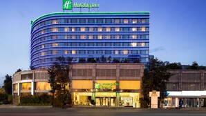 A Holiday Inn hotel with a curved facade, multiple floors, and a prominent green and blue sign. - Holiday Inn Chengdu Century City-EastTower by IHG (Chengdu)