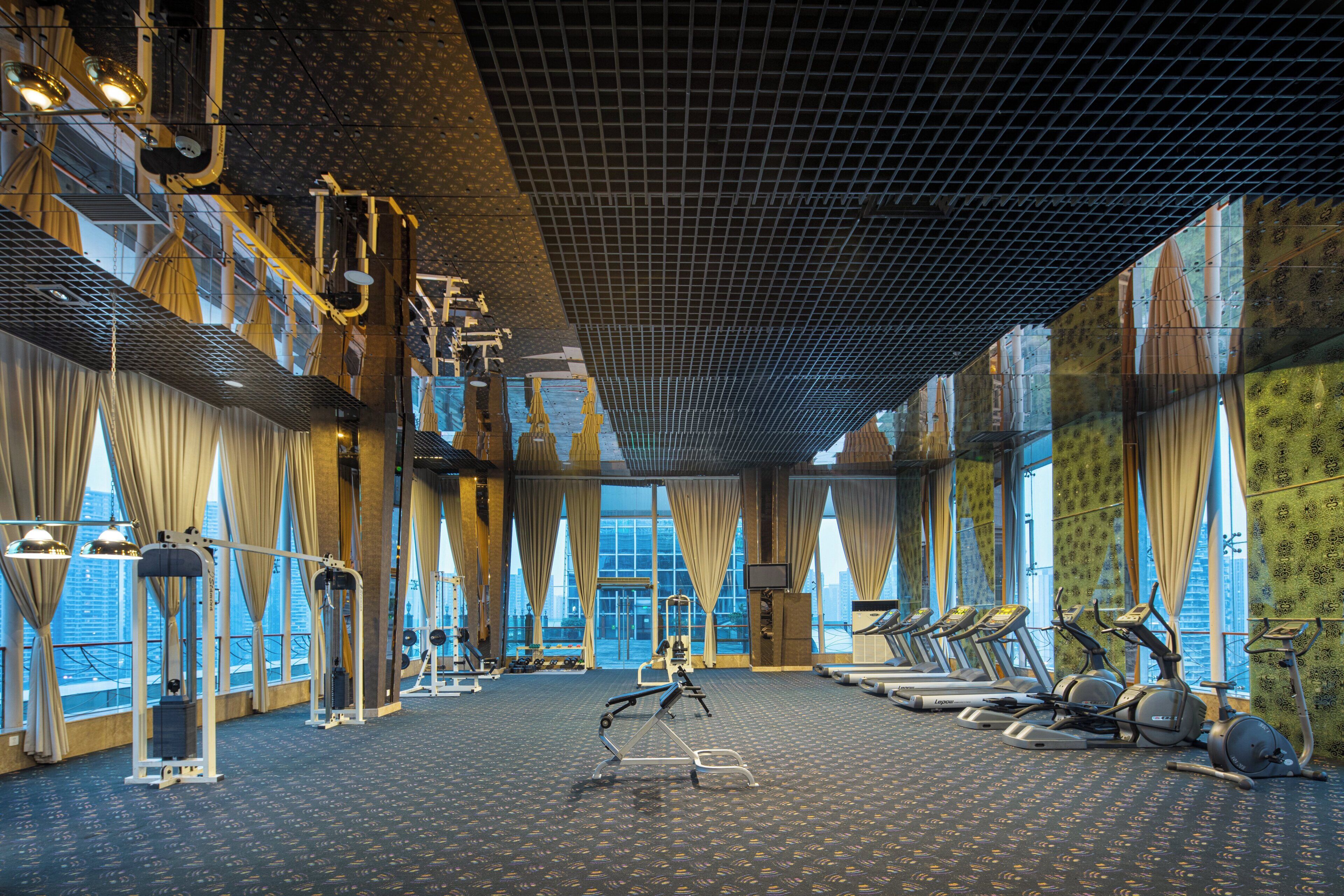 Ein Fitnessstudio mit Trainingsgeräten, großen Fenstern und einem gemusterten Boden.