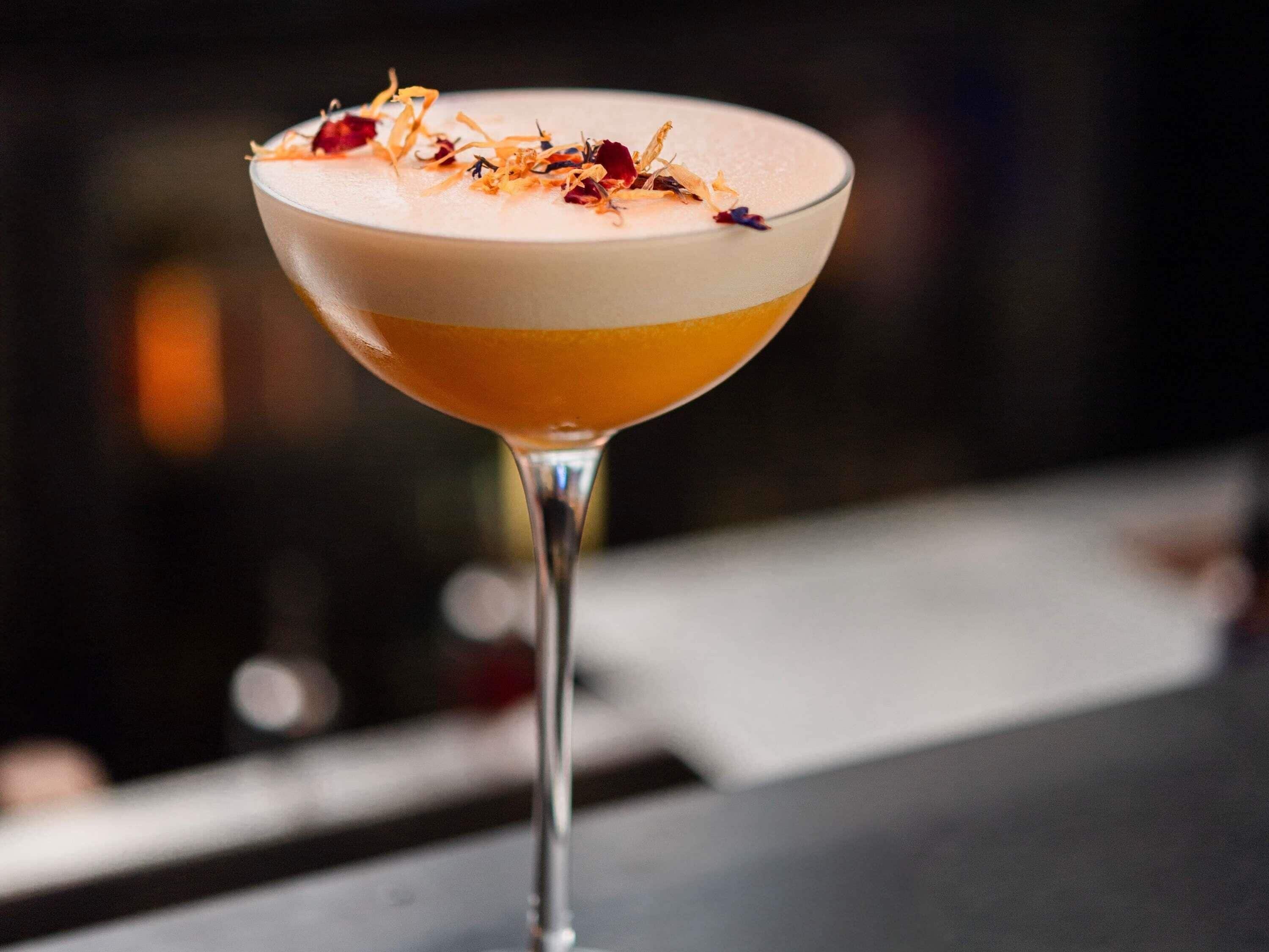 A cocktail in a martini glass with a layered appearance and garnished with dried flowers.