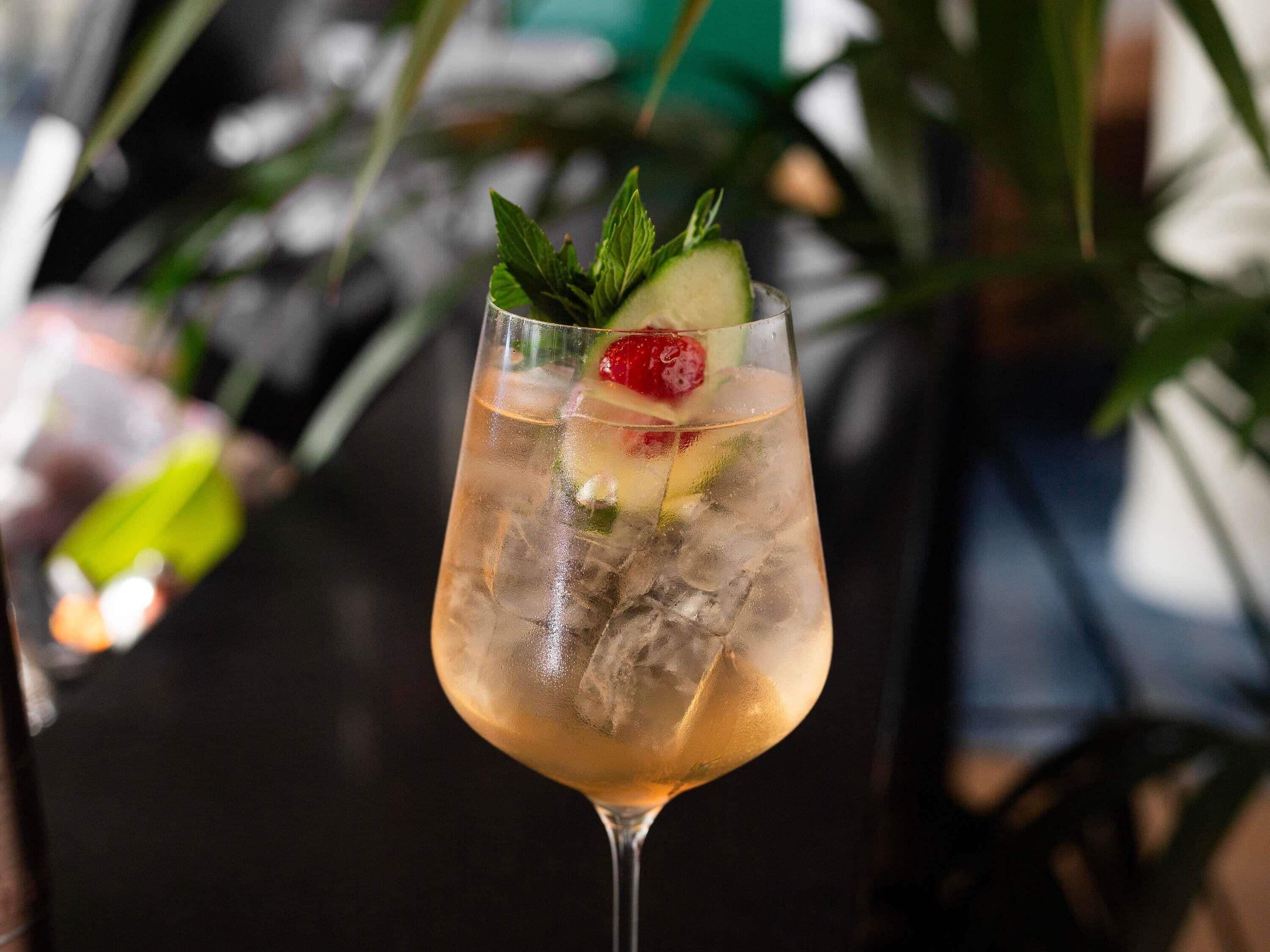 A cocktail glass with ice and garnishes on a table.