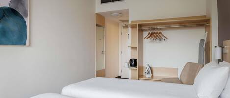 Una habitación de hotel con una cama grande, un armario con espejo, un perchero y una mesita con tetera y tazas.