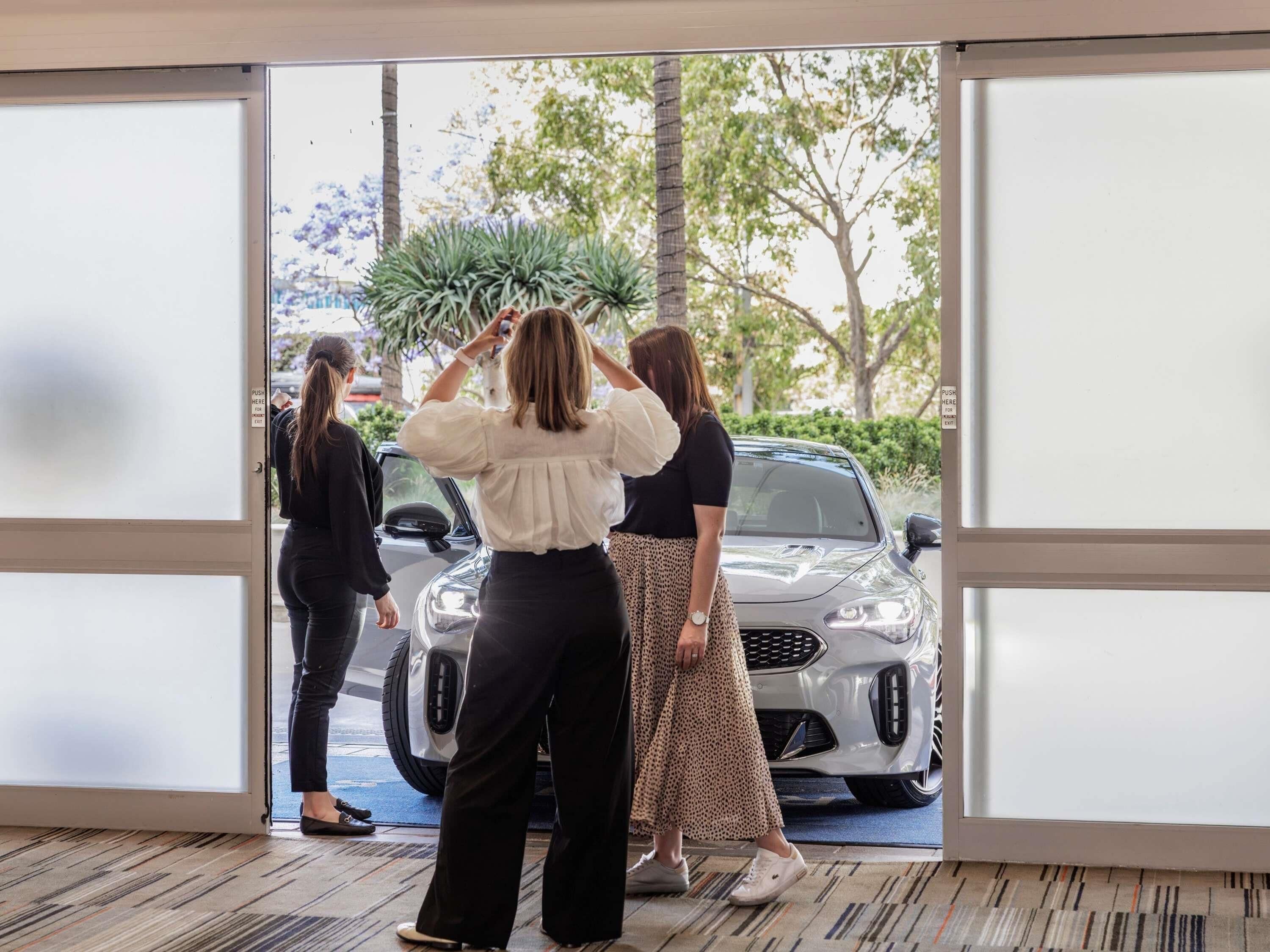 A view through a glass door of a car dealership with a silver car on display.