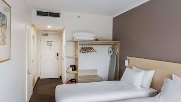 Una habitación de hotel con una cama, un armario, un perchero y una pequeña mesa.