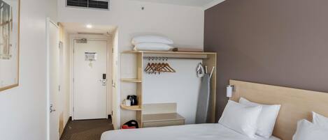 Una habitación de hotel con una cama, un armario, un perchero y una pequeña mesa.