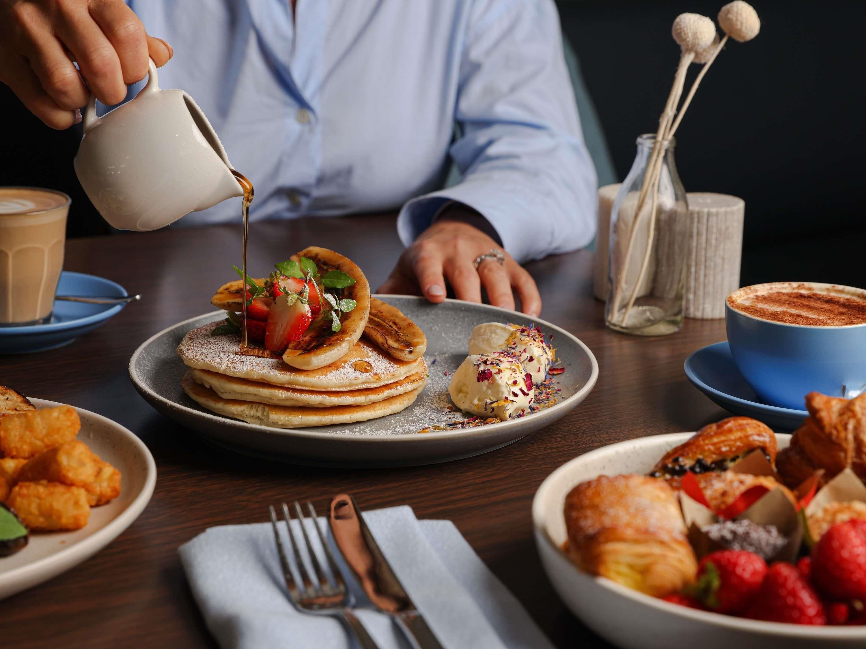 Een ontbijtsetting met pannenkoeken, een kop koffie en een bord gebak.