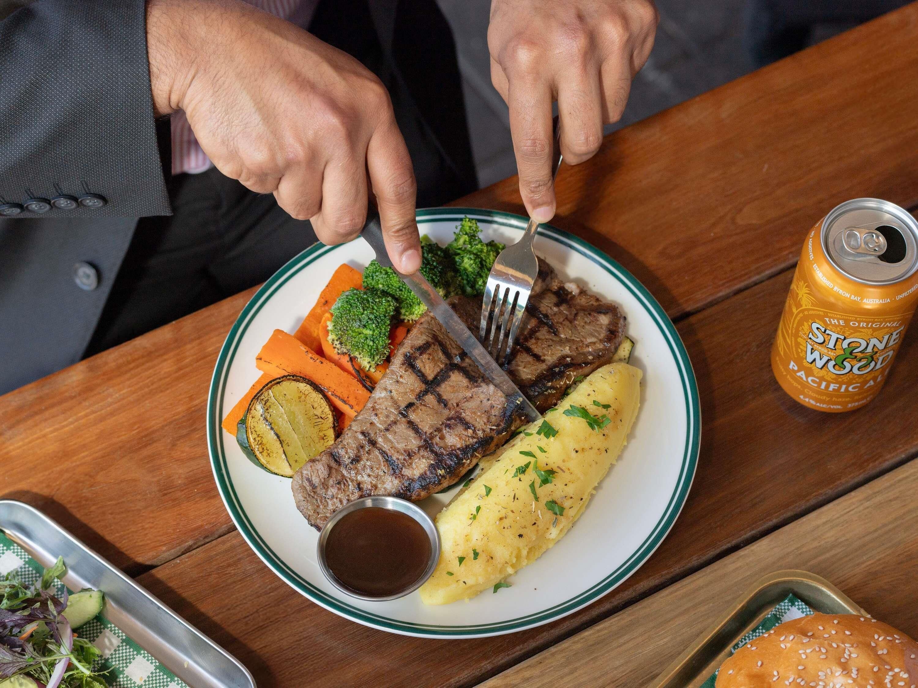 A plate with steak, vegetables, and mashed potatoes, a can of Stone & Wood Pacific Ale, and a small bowl of sauce.