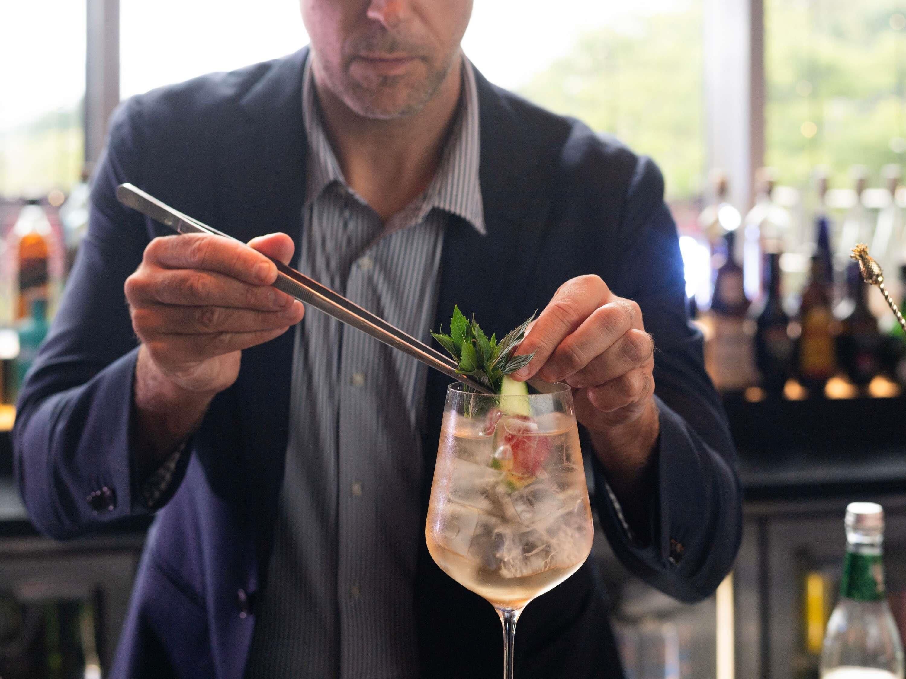 A person preparing a cocktail with a straw and a garnish in a glass.
