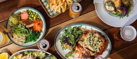 Una mesa con varios platos, incluyendo una hamburguesa, papas fritas, ensalada y un plato de pescado con patatas fritas.