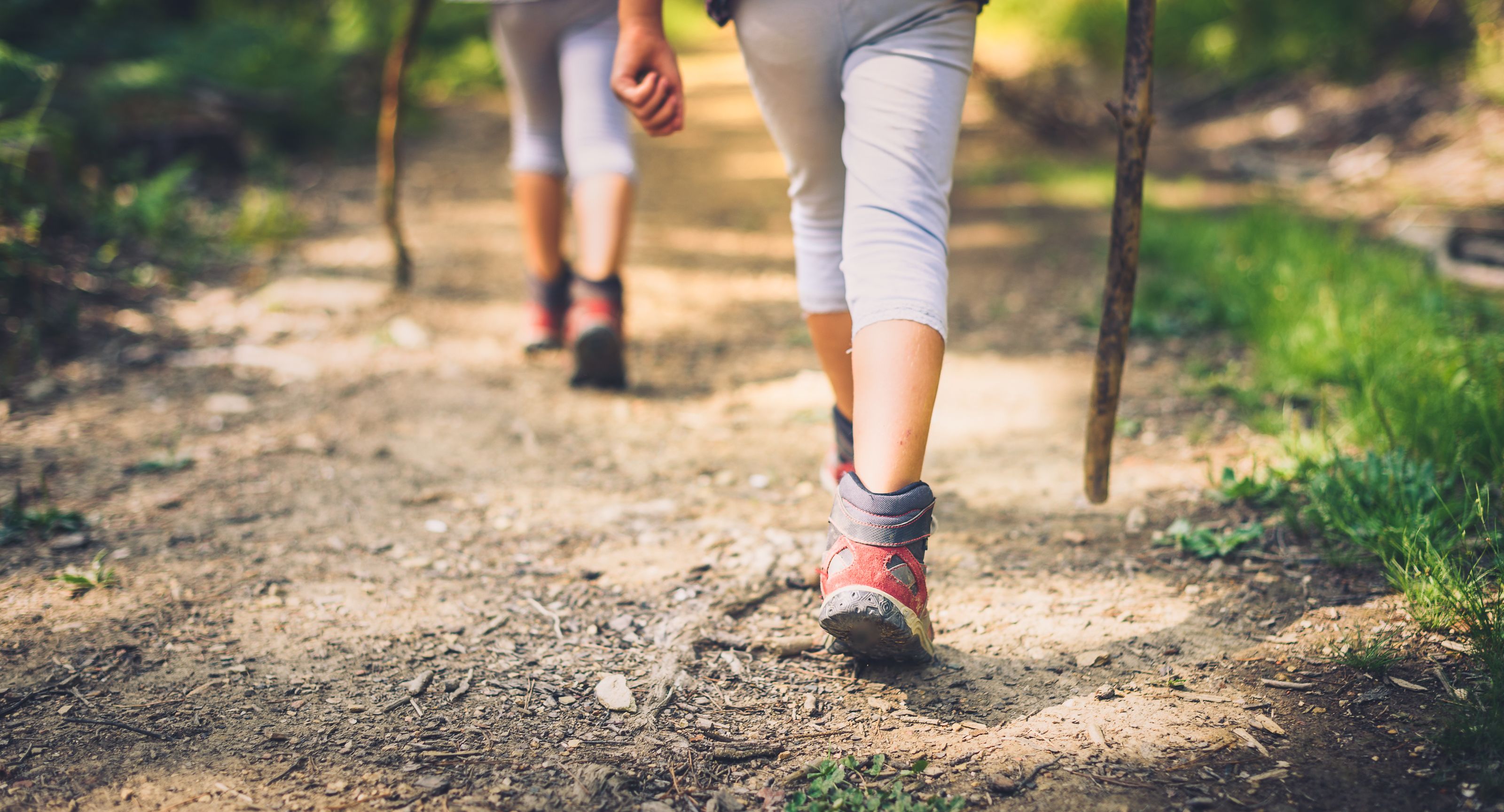A close-up of a person's feet walking on a dirt path, wearing red shoes and grey pants.